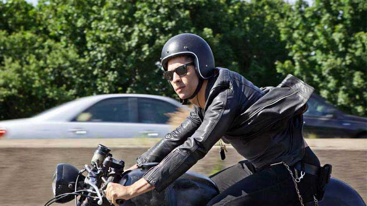 Wearing a helmet, a male motorcycle rider checks for oncoming traffic.